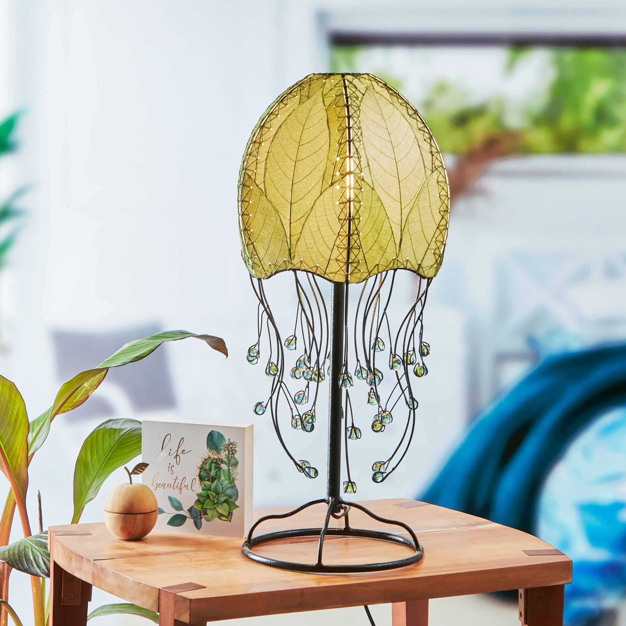In a coastal inspired living room, crafted by the artisans of Eangee Home Design, the Jellyfish Table Lamp in green stands gracefully, featuring fossilized cocoa leaf shade, abaca rope accents, wrought iron frame, handcrafted, adding warmth and character to the space.