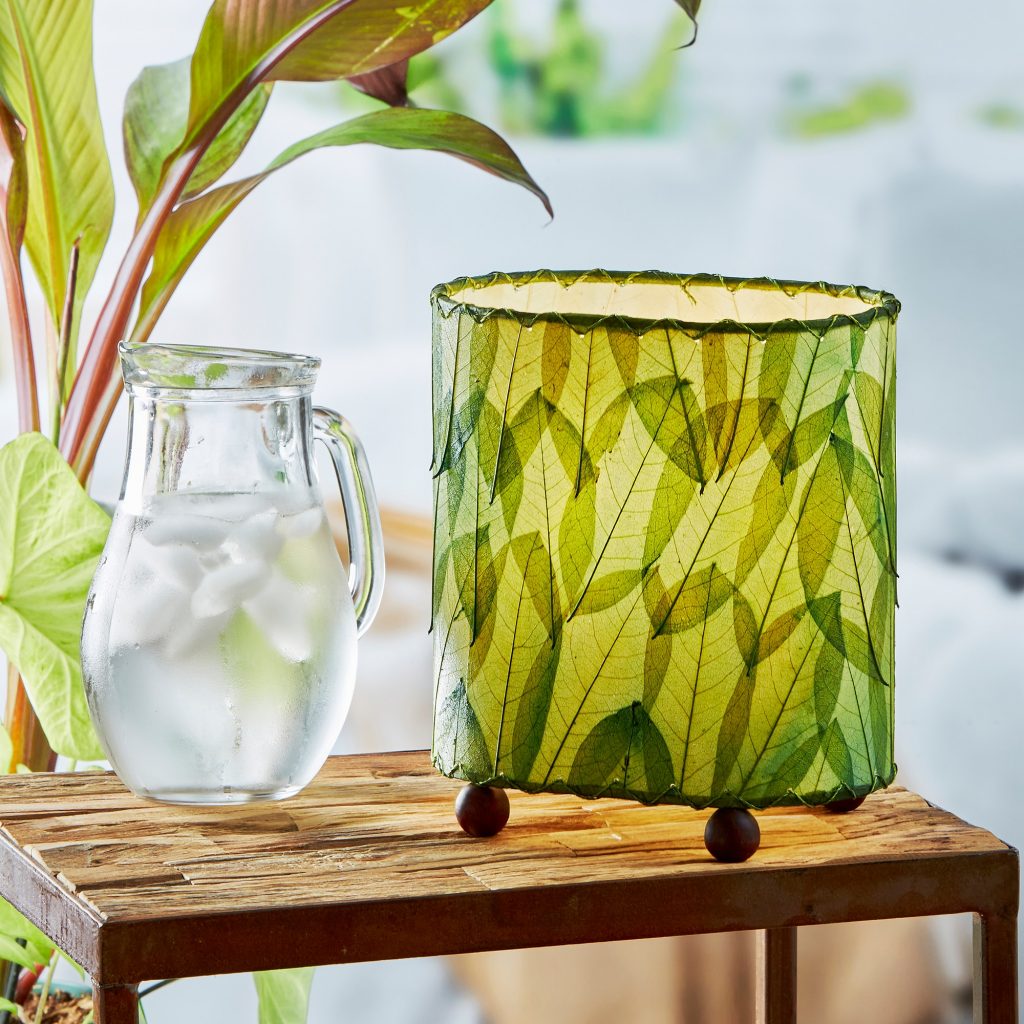 531-g-4-sq-lifestyle In a sun drenched entryway, crafted by the artisans of Eangee Home Design, the Mini Guyabano Table Lamp in green stands gracefully, featuring fossilized cocoa leaf shade, guyabano leaf shade, wrought iron frame, adding warmth and character to the space.