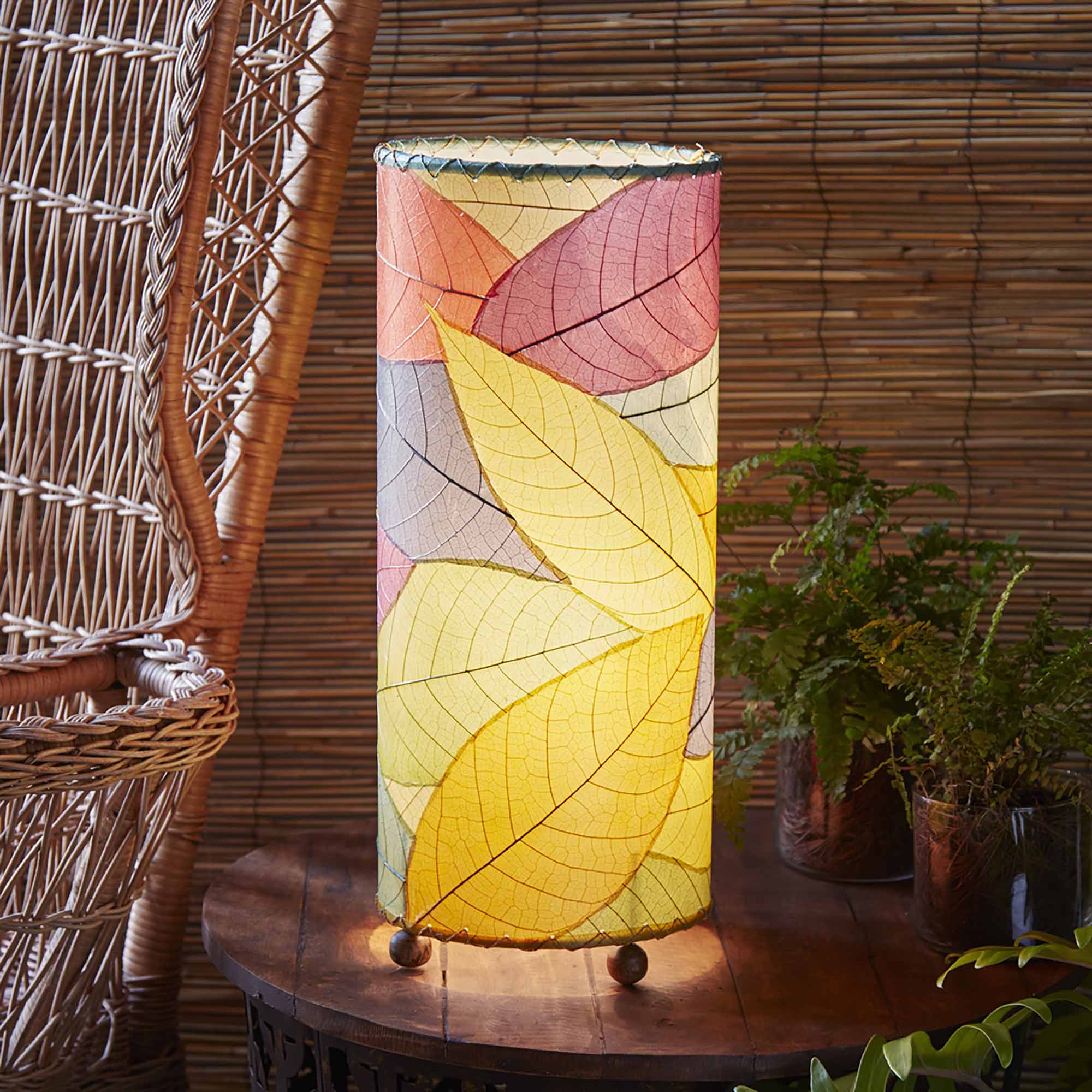 In a modern interior with earth tones, crafted by the artisans of Eangee Home Design, the Cocoa Leaf Cylinder Table Lamp in multi color stands gracefully, featuring fossilized cocoa leaf shade, wrought iron frame, handcrafted, adding warmth and character to the space.
