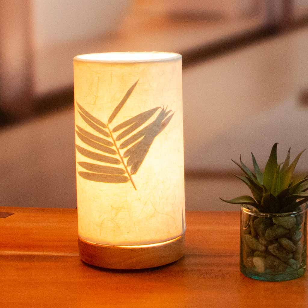 646-a-3-sq-lifestyle In a modern interior with earth tones, crafted by the artisans of Eangee Home Design, the Mini Paper Cylinder Table Lamp Bamboo in natural stands gracefully, featuring reclaimed mango wood base, recycled paper shade, sustainably sourced, recycled materials, adding warmth and character to the space.