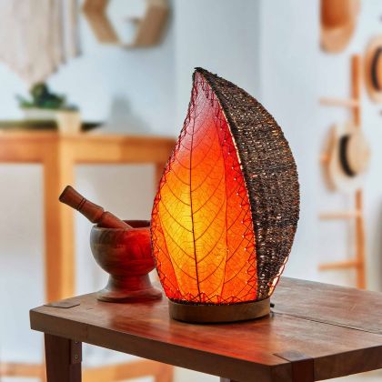 In a quiet bedside corner, crafted by the artisans of Eangee Home Design, the Leaflet Table Lamp in red stands gracefully, featuring fossilized cocoa leaf shade, abaca rope accents, reclaimed mango wood base, wrought iron frame, sustainably sourced, adding warmth and character to the space.
