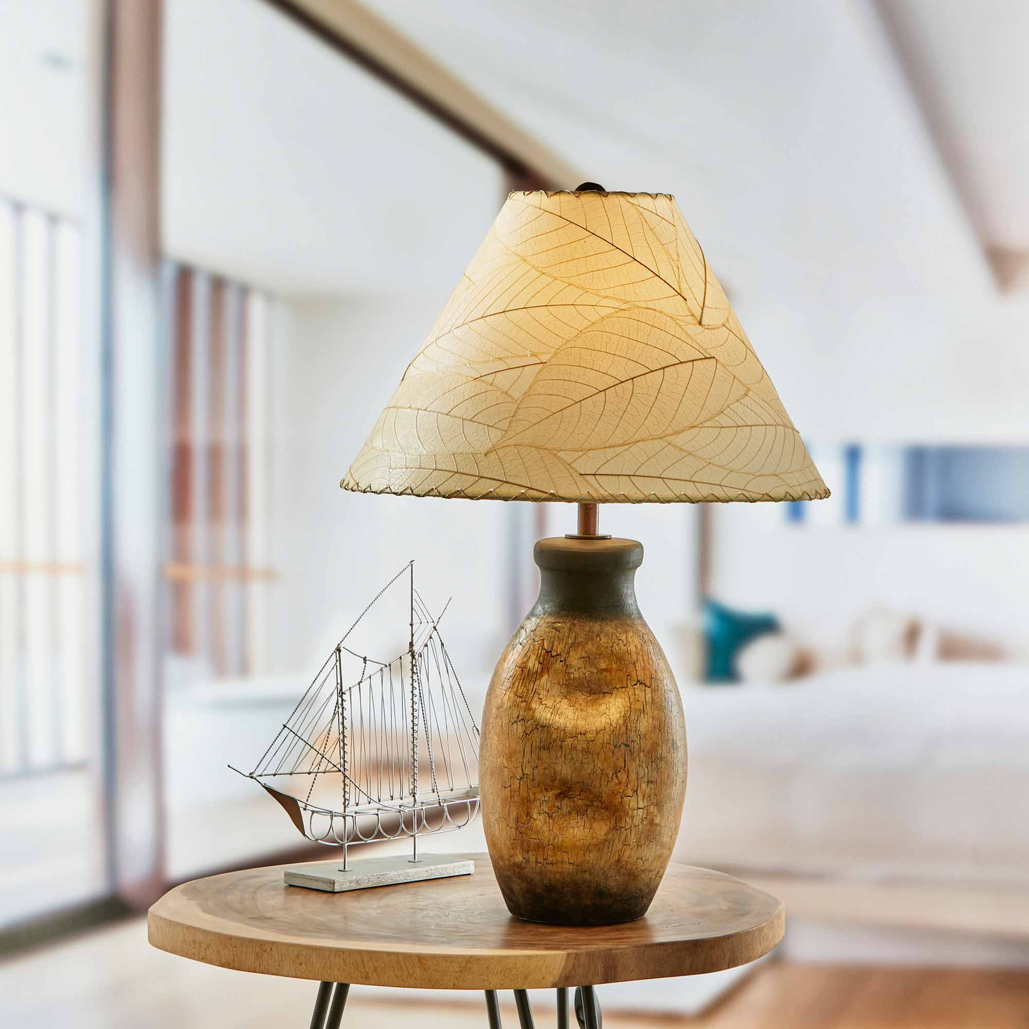 In a softly lit reading nook, crafted by the artisans of Eangee Home Design, the Bell Shade Cocoa in natural stands gracefully, featuring fossilized cocoa leaf shade, wrought iron frame, handcrafted, adding warmth and character to the space.