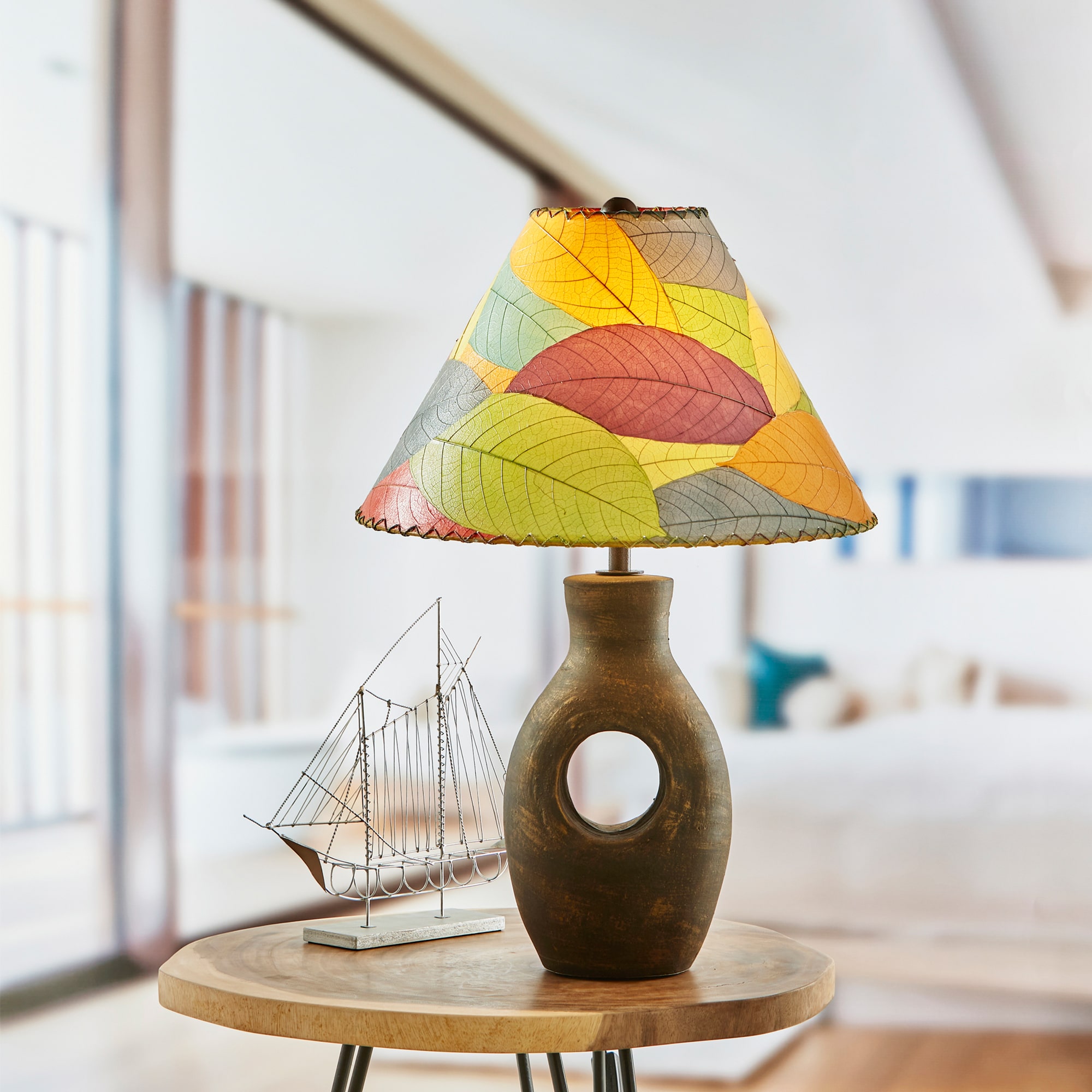 In a coastal inspired living room, crafted by the artisans of Eangee Home Design, the Bell Shade Cocoa in multi color stands gracefully, featuring fossilized cocoa leaf shade, wrought iron frame, handcrafted, adding warmth and character to the space.