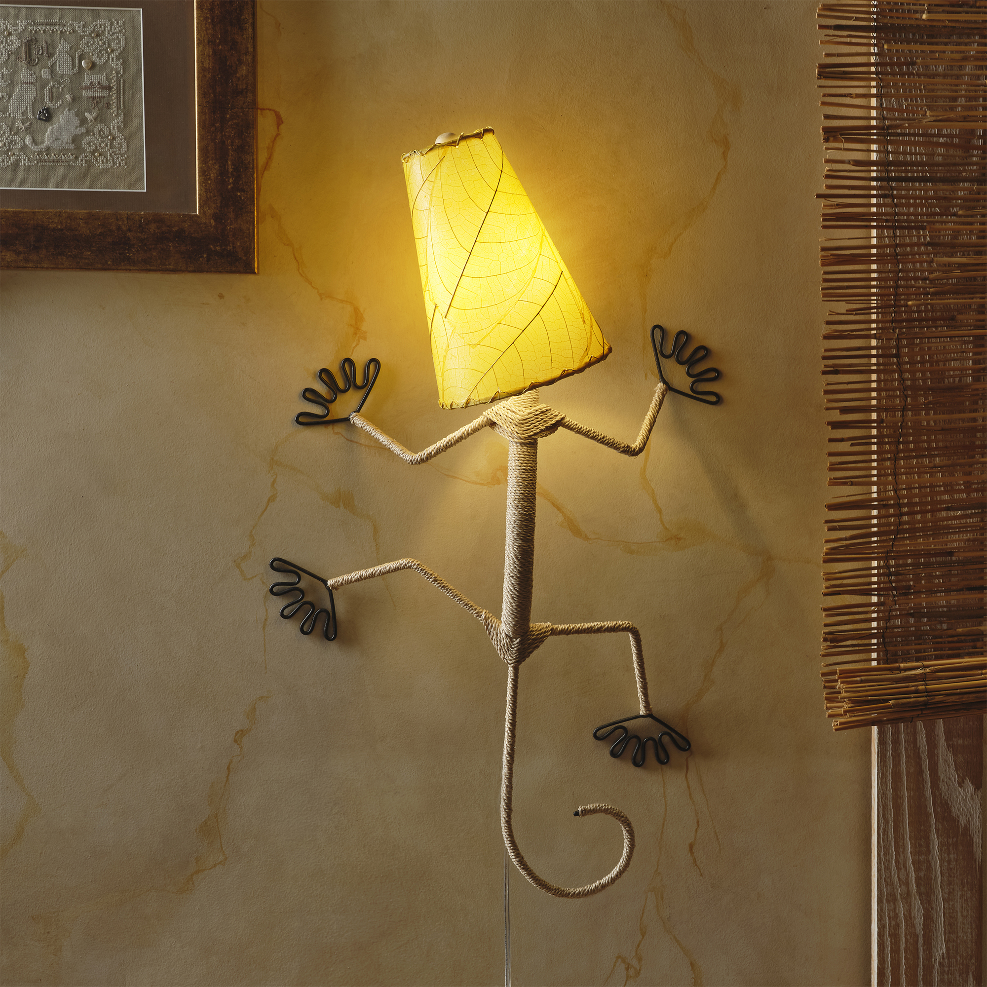 In a softly lit reading nook, crafted by the artisans of Eangee Home Design, the Gecko Wall Lamp Shade in yellow hangs, featuring fossilized cocoa leaf shade, abaca rope accents, wrought iron frame, handcrafted, adding warmth and character to the space.