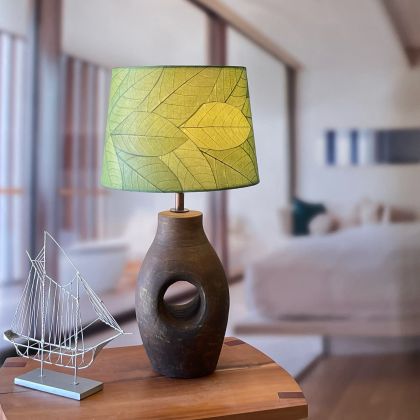 In a modern interior with earth tones, crafted by the artisans of Eangee Home Design, the 14 Inch Tapered Drum Shade in green stands gracefully, featuring fossilized cocoa leaf shade, wrought iron frame, fair trade, eco friendly, sustainably sourced, handcrafted, adding warmth and character to the space.