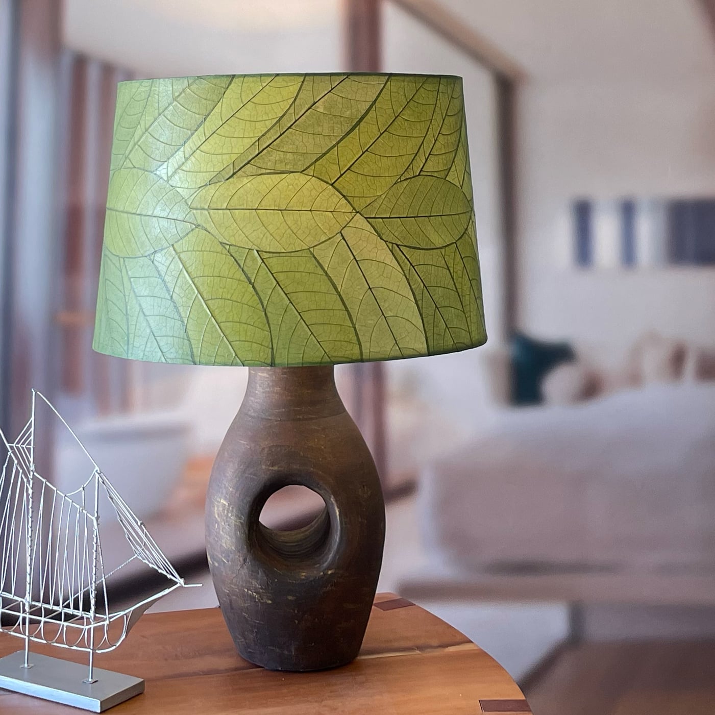 In a sun drenched entryway, crafted by the artisans of Eangee Home Design, the 18 Inch Tapered Drum Shade in green stands gracefully, featuring fossilized cocoa leaf shade, wrought iron frame, eco friendly, sustainably sourced, adding warmth and character to the space.