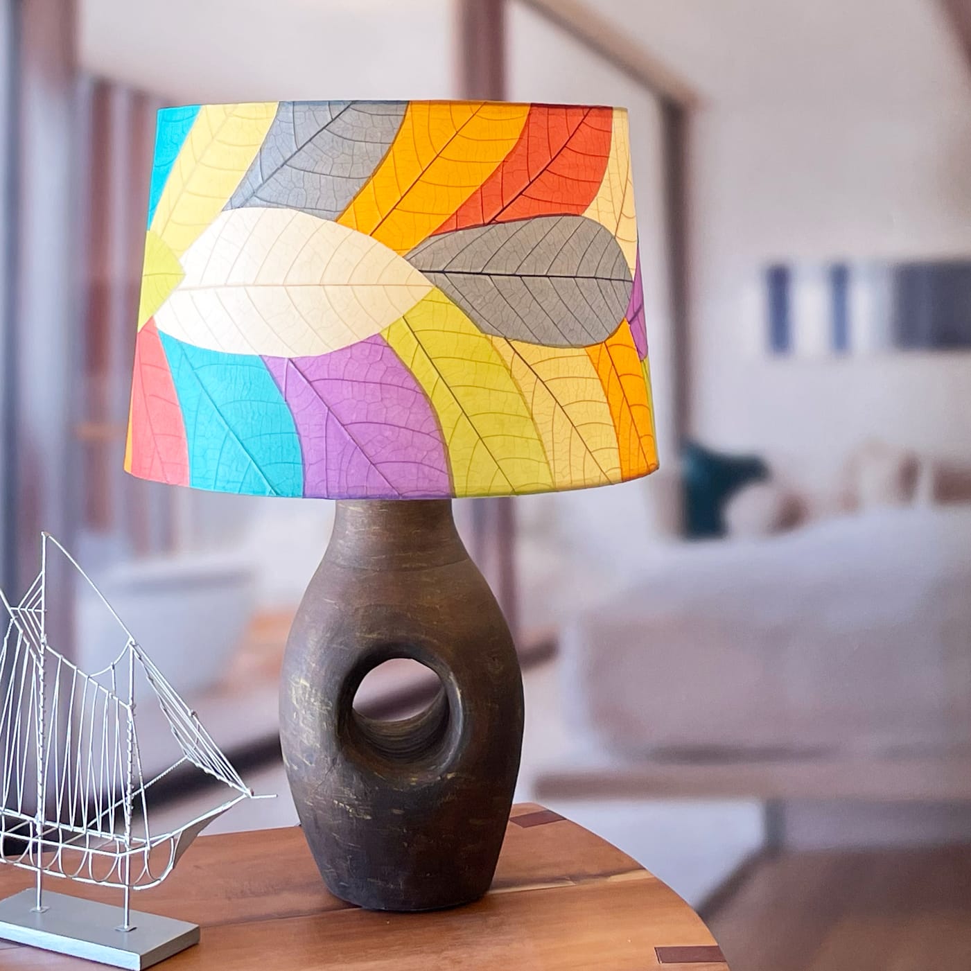 In a modern interior with earth tones, crafted by the artisans of Eangee Home Design, the 18 Inch Tapered Drum Shade in multi color stands gracefully, featuring fossilized cocoa leaf shade, wrought iron frame, eco friendly, sustainably sourced, adding warmth and character to the space.