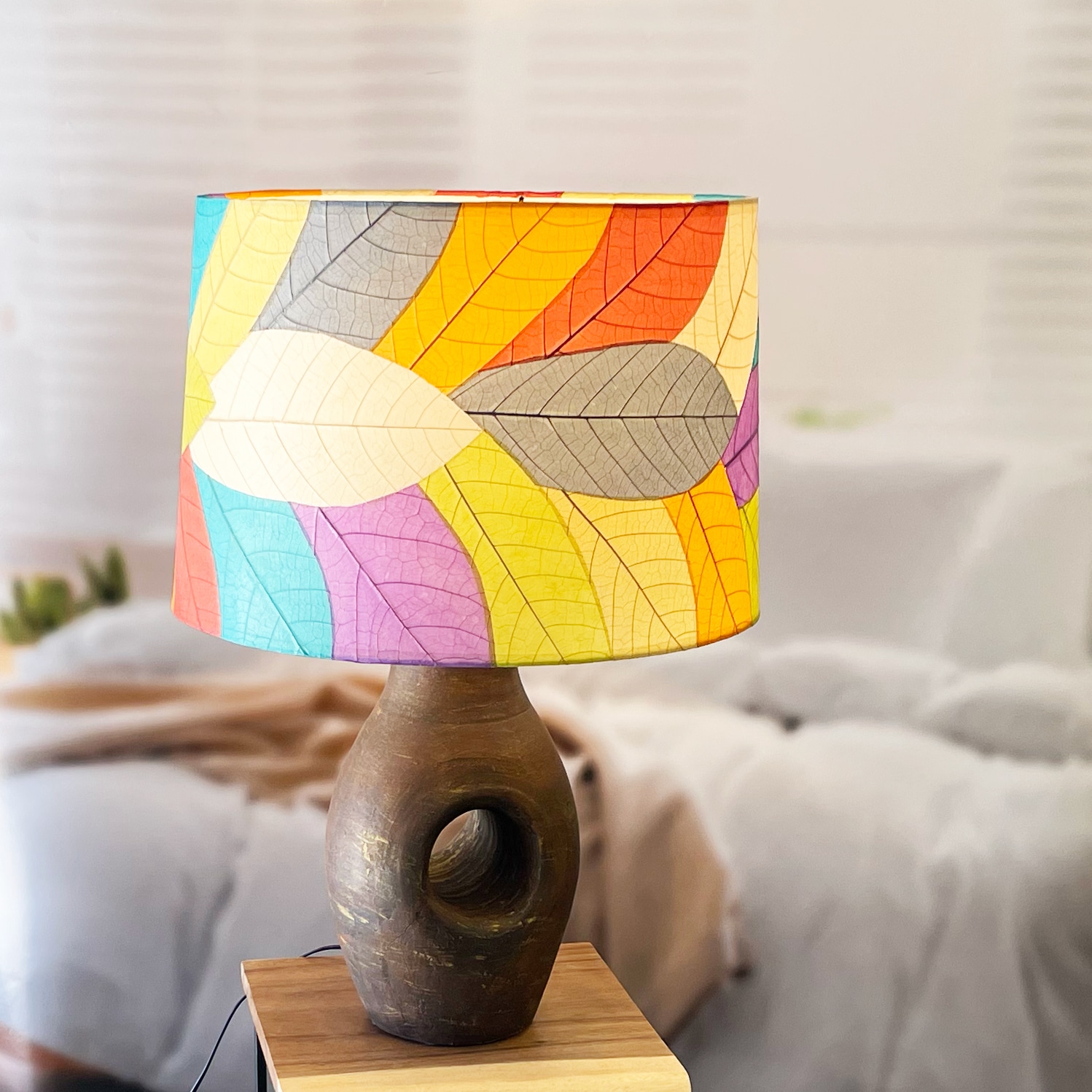 In a modern interior with earth tones, crafted by the artisans of Eangee Home Design, the 18 Inch Tapered Drum Shade in multi color stands gracefully, featuring fossilized cocoa leaf shade, wrought iron frame, eco friendly, sustainably sourced, adding warmth and character to the space.