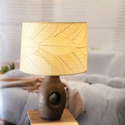 In a sun drenched entryway, crafted by the artisans of Eangee Home Design, the 18 Inch Tapered Drum Shade in natural stands gracefully, featuring fossilized cocoa leaf shade, wrought iron frame, eco friendly, sustainably sourced, adding warmth and character to the space.