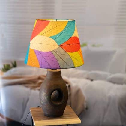 In a modern interior with earth tones, crafted by the artisans of Eangee Home Design, the 16 Inch British Empire Shade in multi color stands gracefully, featuring fossilized cocoa leaf shade, wrought iron frame, fair trade, eco friendly, sustainably sourced, adding warmth and character to the space.