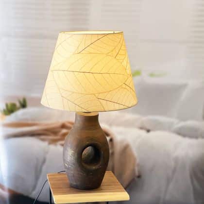 In a minimalist loft with natural textures, crafted by the artisans of Eangee Home Design, the 16 Inch British Empire Shade in natural stands gracefully, featuring fossilized cocoa leaf shade, wrought iron frame, fair trade, eco friendly, sustainably sourced, adding warmth and character to the space.