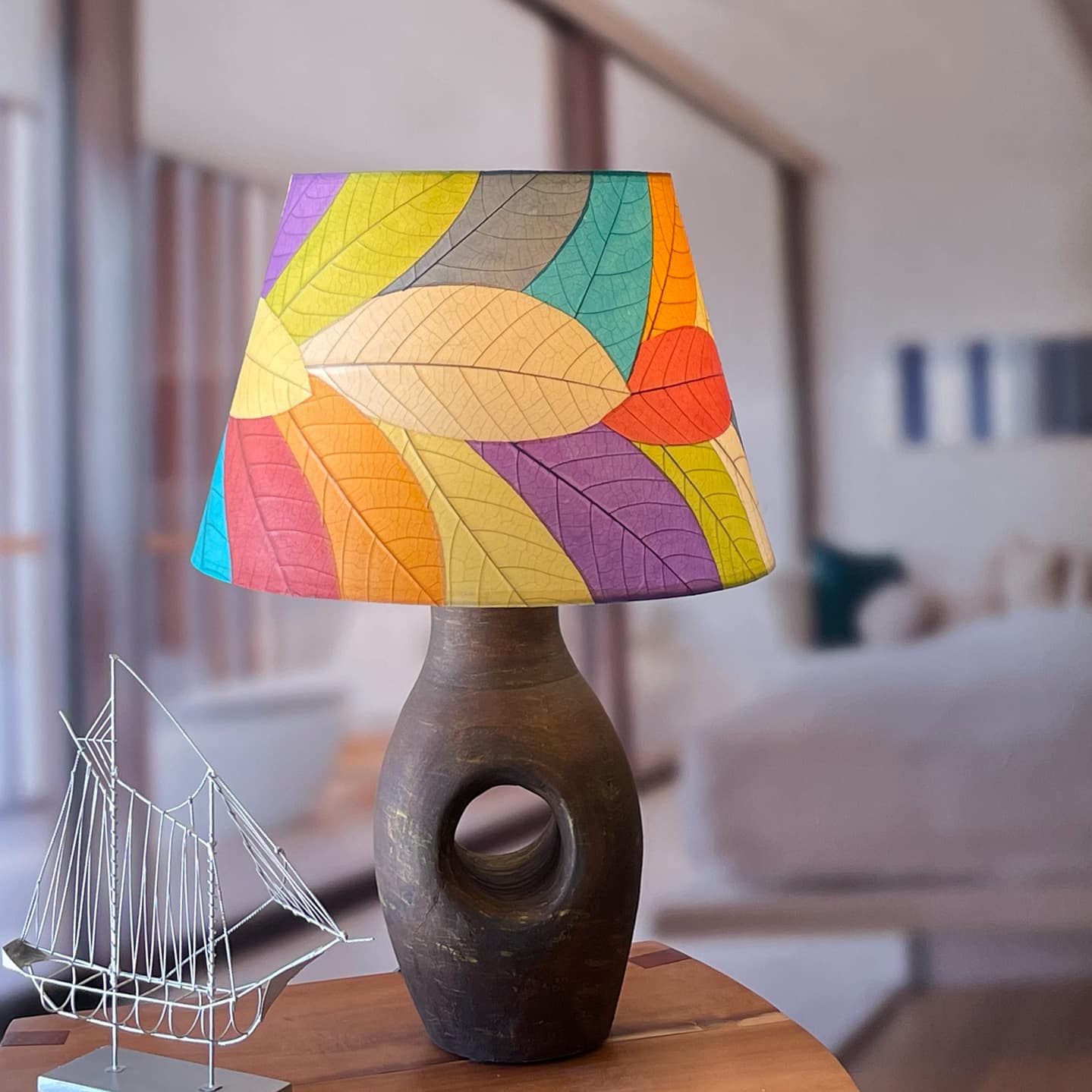 In a modern interior with earth tones, crafted by the artisans of Eangee Home Design, the 18 Inch British Empire Shade in multi color stands gracefully, featuring fossilized cocoa leaf shade, wrought iron frame, eco friendly, sustainably sourced, adding warmth and character to the space.