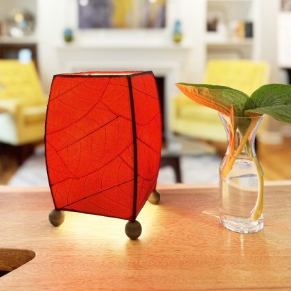 On a writing desk, the Mini Square Cocoa Leaf Table crafted by the artisans of Eangee Home Design Lamp in red finish by Eangee Home Design glows softly, its fossilized cocoa leaf panels, wrought iron frame, and hand placed natural leaves bringing it's the warm, inviting glow that draws you in first.