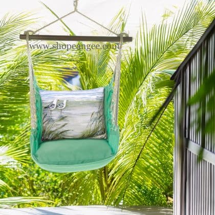 In a shaded porch swing a green outdoor swing crafted by the artisans of Magnolia Casual called the Swing Set 4 piece Seafoam Green Solid w/ Seagulls is displayed featuring 100 percent weather resistant fabric, weather resistant polyester fabric, handcrafted adding comfort and style to the space featuring shades of green.