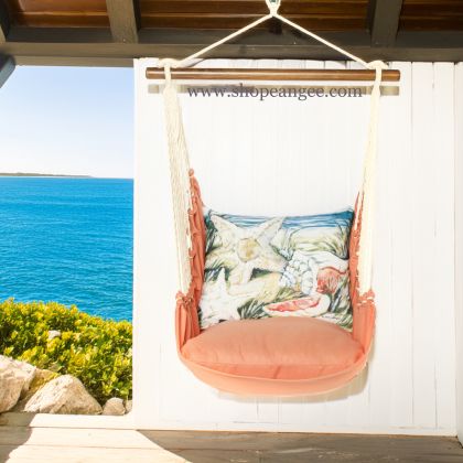 In a shaded porch swing a multi colored outdoor swing crafted by the artisans of Magnolia Casual called the Swing Set 4 piece Living Coral w/ Seashells is displayed featuring 100 percent weather resistant fabric, weather resistant polyester fabric, handcrafted adding comfort and style to the space featuring with a coral motif and shades of coral.