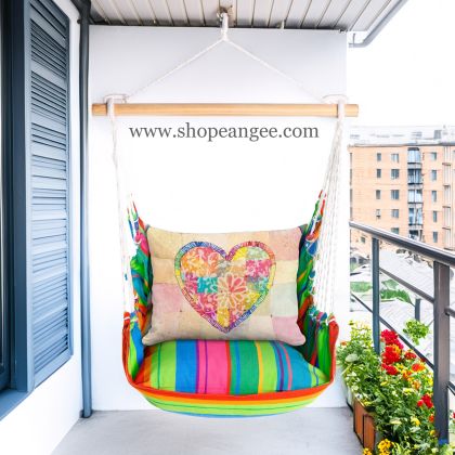 In a shaded porch swing a multi colored outdoor swing crafted by the artisans of Magnolia Casual called the Swing Set 4 piece Le Jardin Nouveau w/ Colorful Heart is displayed featuring 100 percent weather resistant fabric, weather resistant polyester fabric, handcrafted adding comfort and style to the space.