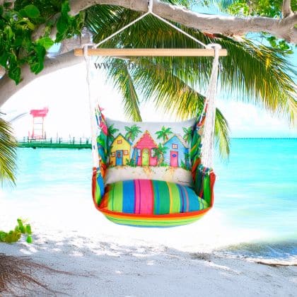 In a shaded porch swing a multi colored outdoor swing crafted by the artisans of Magnolia Casual called the Swing Set 4 piece Le Jardin Nouveau w/ Colorful Beach Cottages is displayed featuring 100 percent weather resistant fabric, weather resistant polyester fabric, handcrafted adding comfort and style to the space.