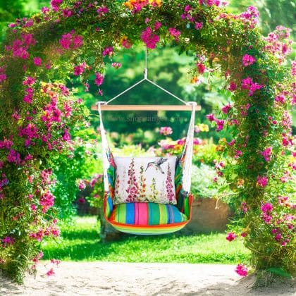 In a cozy garden seating area a multi colored outdoor swing crafted by the artisans of Magnolia Casual called the Swing Set 4 piece Le Jardin Nouveau w/ Foxgloves with Hummingbird is displayed featuring 100 percent weather resistant fabric, weather resistant polyester fabric, handcrafted adding comfort and style to the space featuring with a hummingbird motif.
