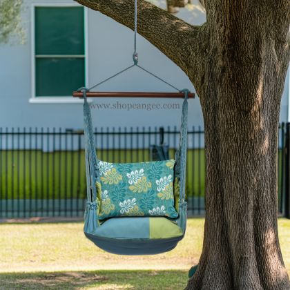 In an outdoor reading nook a multi colored outdoor swing crafted by the artisans of Magnolia Casual called the Swing Set 4 piece Meadow Mist Stripe w/ Tropical Flow is displayed featuring 100 percent weather resistant fabric, weather resistant polyester fabric, handcrafted, natural materials adding comfort and style to the space featuring with a stripe motif.