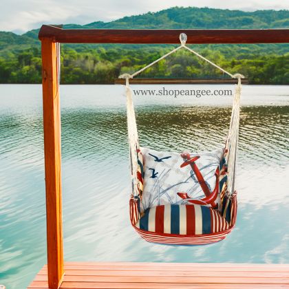 In a poolside chaise a red outdoor swing crafted by the artisans of Magnolia Casual called the Swing Set 4 piece Stars & Stripes w/ Red Anchor is displayed featuring 100 percent weather resistant fabric, weather resistant polyester fabric, handcrafted adding comfort and style to the space featuring with a stripes motif and shades of red.