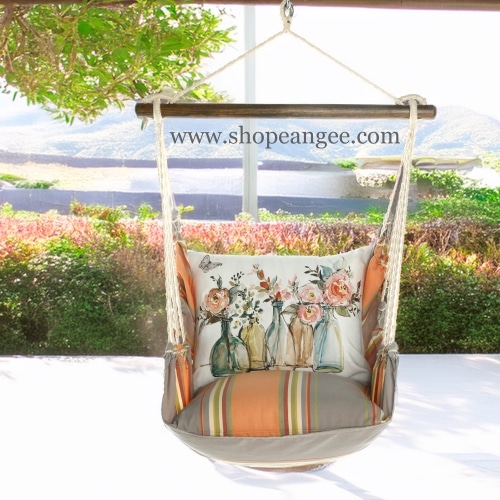In a cozy garden seating area a multi colored outdoor swing crafted by the artisans of Magnolia Casual called the Swing Set 4 piece Serene Sunset w/ Flowers in Glass Bottles is displayed featuring 100 percent weather resistant fabric, weather resistant polyester fabric, handcrafted adding comfort and style to the space.