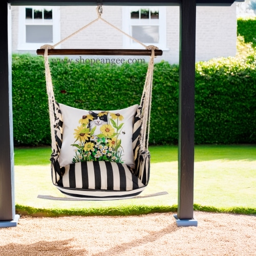 In an outdoor reading nook a black outdoor swing crafted by the artisans of Magnolia Casual called the Swing Set 4 piece True Black Stripe w/ Cat with Daisies is displayed featuring 100 percent weather resistant fabric, weather resistant polyester fabric, handcrafted adding comfort and style to the space featuring with a stripe motif and shades of black.