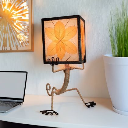 Gecko?shaped table lamp crafted by Eangee Home Design with orange fossilized cocoa?leaf panels hand?stitched onto a wrought?iron frame; playful gecko silhouette hugs the shade, and warm light spills through every vein; eco?friendly, artisan?crafted design