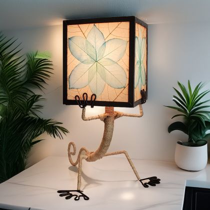 In a quiet bedside corner, crafted by the artisans of Eangee Home Design, the Enlightened Gecko Table Lamp in sea blue stands gracefully, featuring fossilized cocoa leaf shade, guyabano leaf shade, abaca rope accents, wrought iron frame, handcrafted, adding warmth and character to the space.