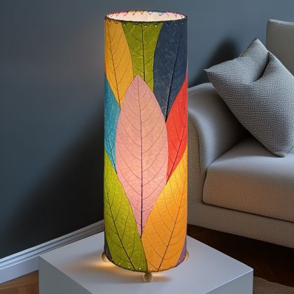 In a softly lit reading nook, crafted by the artisans of Eangee Home Design, the 24 Inch Cocoa Leaf Cylinder Table Lamp in multi color stands gracefully, featuring fossilized cocoa leaf shade, fair trade, eco friendly, sustainably sourced, handcrafted, adding warmth and character to the space.