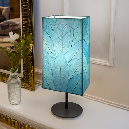 In a sun drenched entryway, crafted by the artisans of Eangee Home Design, the Sequoia Table Lamp in sea blue stands gracefully, featuring fossilized cocoa leaf shade, fair trade, sustainably sourced, adding warmth and character to the space.