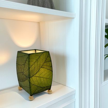 On a floating shelf, the Mini Square Cocoa Leaf Table crafted by the artisans of Eangee Home Design Lamp in green finish by Eangee Home Design glows softly, its fossilized cocoa leaf panels, wrought iron frame, and hand placed natural leaves bringing it's the warm, inviting glow that draws you in first.