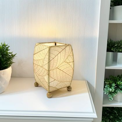 On a floating shelf, the Mini Square Cocoa Leaf Table crafted by the artisans of Eangee Home Design Lamp in natural finish by Eangee Home Design glows softly, its fossilized cocoa leaf panels, wrought iron frame, and hand placed natural leaves bringing it's the warm, inviting glow that draws you in first.