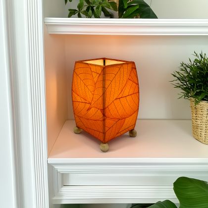 Crafted by the artisans of Eangee Home Design, the Mini Square Cocoa Leaf Table Lamp in orange against a clean backdrop, featuring fossilized cocoa leaf shade, wrought iron frame, fair trade, eco friendly, sustainably sourced, handcrafted.