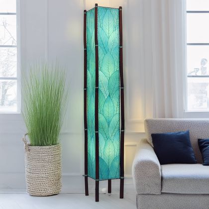 In a modern living room, the Fortune Giant Floor crafted by the artisans of Eangee Home Design Lamp in sea blue finish by Eangee Home Design stands tall, its fossilized cocoa leaf panels, abaca twine accents, rattan legs, powder coated wrought iron frame, wrought iron frame, hand placed natural leaves, hand placed leaf panels, and abaca twine stitching casting a warm glow that some pieces don't just fill a space they define it.