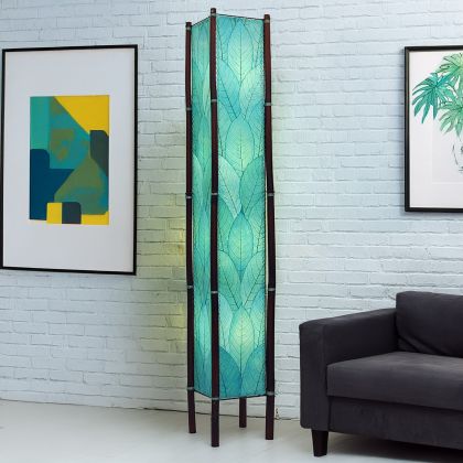 In a softly lit reading nook, crafted by the artisans of Eangee Home Design, the Fortune Giant Floor Lamp in sea blue stands gracefully, featuring fossilized cocoa leaf shade, abaca rope accents, rattan leg supports, wrought iron frame, eco friendly, adding warmth and character to the space.