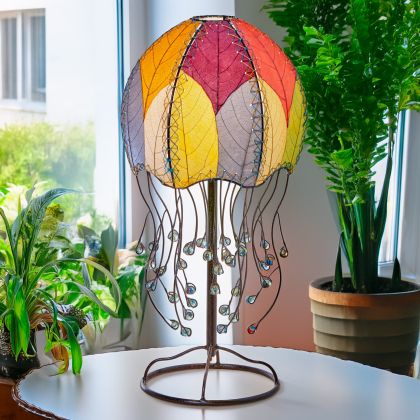 Jellyfish?inspired table lamp crafted by Eangee Home Design draped in multi color cocoa?leaf panels that flow like tentacles; underwater feel enhanced as glowing light pours against the leaf?veined surface; sustainably handcrafted by skilled artisans