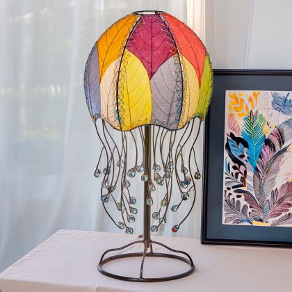 In a coastal inspired living room, crafted by the artisans of Eangee Home Design, the Jellyfish Table Lamp in multi color stands gracefully, featuring fossilized cocoa leaf shade, abaca rope accents, wrought iron frame, handcrafted, adding warmth and character to the space.