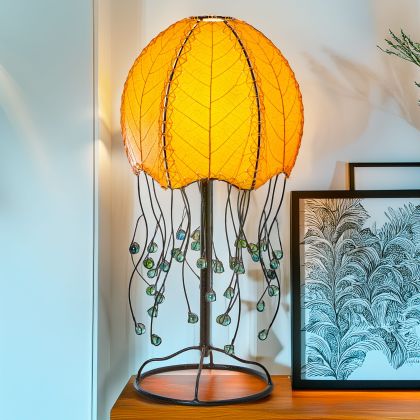 In a quiet bedside corner, crafted by the artisans of Eangee Home Design, the Jellyfish Table Lamp in orange stands gracefully, featuring fossilized cocoa leaf shade, abaca rope accents, wrought iron frame, handcrafted, adding warmth and character to the space.