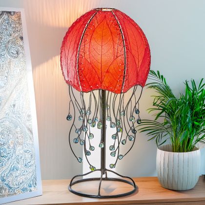In a modern interior with earth tones, crafted by the artisans of Eangee Home Design, the Jellyfish Table Lamp in red stands gracefully, featuring fossilized cocoa leaf shade, abaca rope accents, wrought iron frame, handcrafted, adding warmth and character to the space.