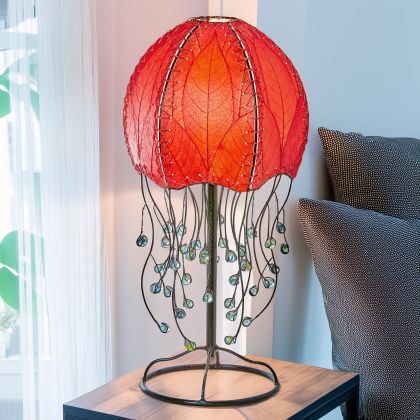 Jellyfish?inspired table lamp crafted by Eangee Home Design draped in red cocoa?leaf panels that flow like tentacles; underwater feel enhanced as warm light radiates through organic leaf texture; handcrafted sustainably by fair?trade artisans