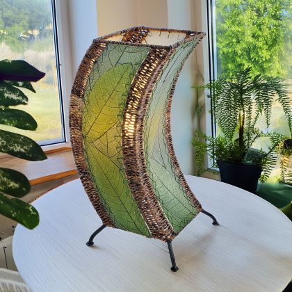 In a quiet bedside corner, crafted by the artisans of Eangee Home Design, the C Shape Table Lamp in green stands gracefully, featuring fossilized cocoa leaf shade, abaca rope accents, fair trade, handcrafted, adding warmth and character to the space.