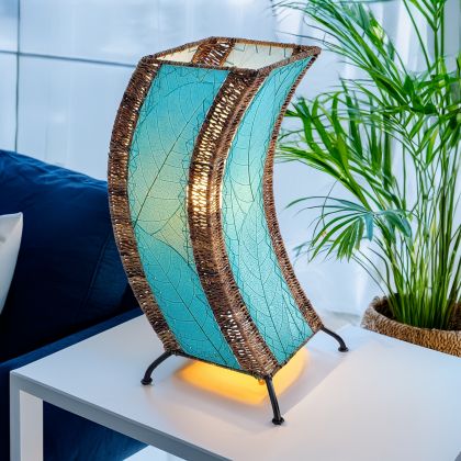 In a sun drenched entryway, crafted by the artisans of Eangee Home Design, the C Shape Table Lamp in sea blue stands gracefully, featuring fossilized cocoa leaf shade, abaca rope accents, fair trade, handcrafted, adding warmth and character to the space.