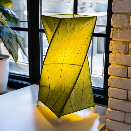 Crafted by the artisans of Eangee Home Design, the Twist Table Lamp in green against a clean backdrop, featuring fossilized cocoa leaf shade, wrought iron frame, handcrafted.