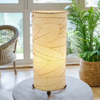 In a sun drenched entryway, crafted by the artisans of Eangee Home Design, the Cocoa Leaf Cylinder Table Lamp in natural stands gracefully, featuring fossilized cocoa leaf shade, wrought iron frame, handcrafted, adding warmth and character to the space.