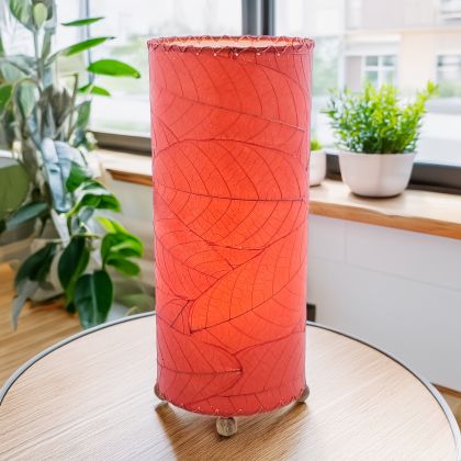 In a modern interior with earth tones, crafted by the artisans of Eangee Home Design, the Cocoa Leaf Cylinder Table Lamp in red stands gracefully, featuring fossilized cocoa leaf shade, wrought iron frame, handcrafted, adding warmth and character to the space.