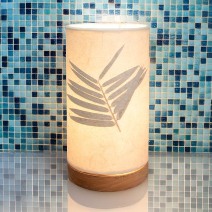 In a coastal inspired living room, crafted by the artisans of Eangee Home Design, the Mini Paper Cylinder Table Lamp Bamboo in natural stands gracefully, featuring reclaimed mango wood base, recycled paper shade, sustainably sourced, recycled materials, adding warmth and character to the space.