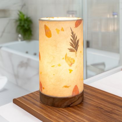 In a modern interior with earth tones, crafted by the artisans of Eangee Home Design, the Mini Paper Cylinder Table Lamp Fern in natural stands gracefully, featuring reclaimed mango wood base, recycled paper shade, sustainably sourced, recycled materials, adding warmth and character to the space.