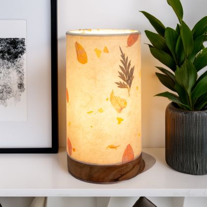 In a quiet bedside corner, crafted by the artisans of Eangee Home Design, the Mini Paper Cylinder Table Lamp Fern in natural stands gracefully, featuring reclaimed mango wood base, recycled paper shade, sustainably sourced, recycled materials, adding warmth and character to the space.