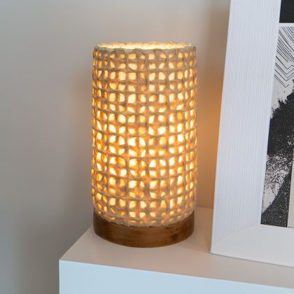 In a quiet bedside corner, crafted by the artisans of Eangee Home Design, the Mini Paper Cylinder Table Lamp Mesh in natural stands gracefully, featuring reclaimed mango wood base, recycled paper shade, sustainably sourced, recycled materials, adding warmth and character to the space.