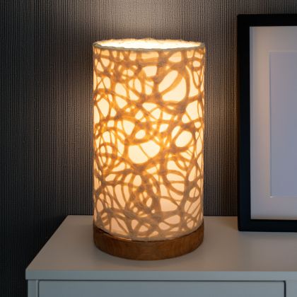 In a coastal inspired living room, crafted by the artisans of Eangee Home Design, the Mini Paper Cylinder Table Lamp Swirl in natural stands gracefully, featuring reclaimed mango wood base, recycled paper shade, sustainably sourced, recycled materials, adding warmth and character to the space.